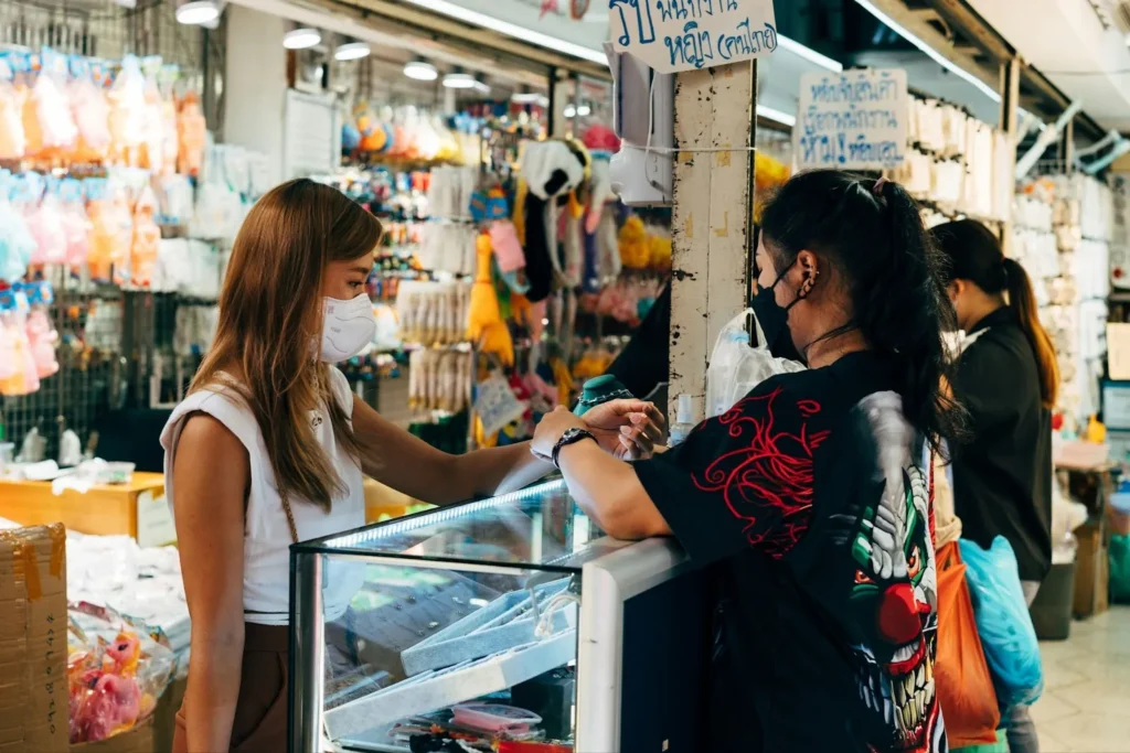 A woman trying on a bracelet and asking for its price to the sales lady

