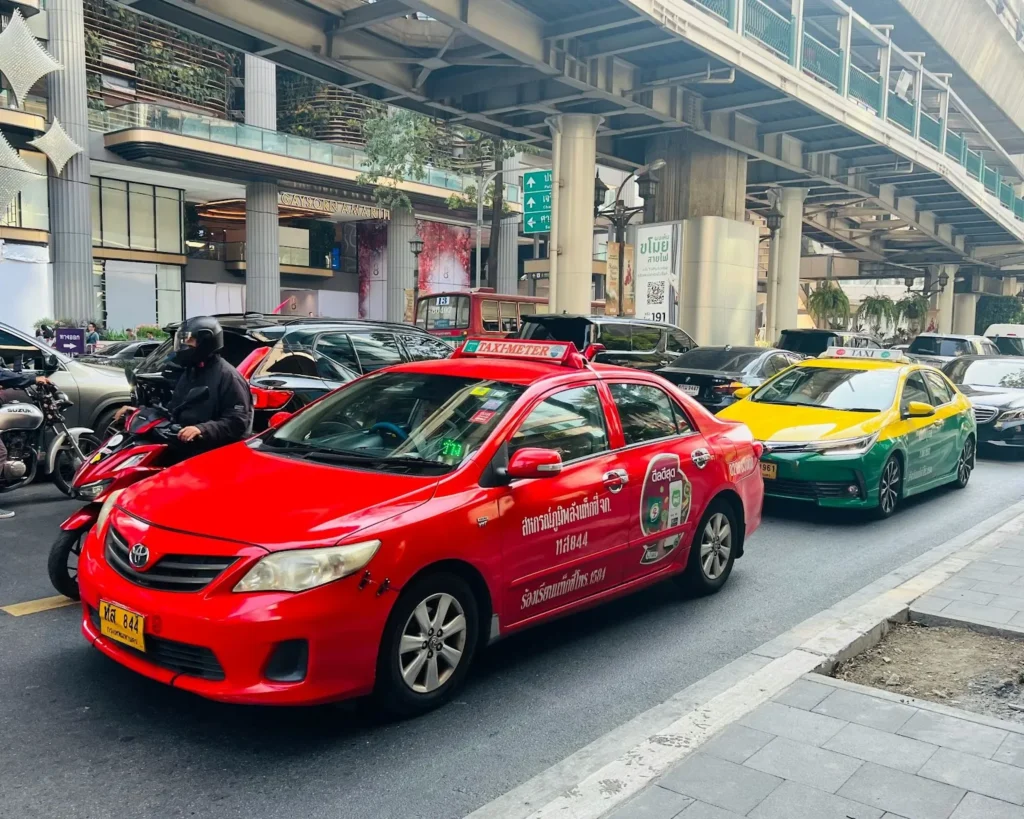 A red metered taxi and another one behind in yellow and green hue driving along the traffic road in Bangkok