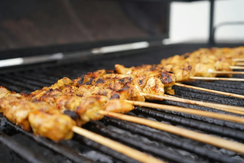 Several skewered pork meat grilling on top of a griller